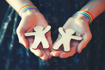 female hands with LGBT rainbow ribbon wristbands holding couple of mini toy wooden men