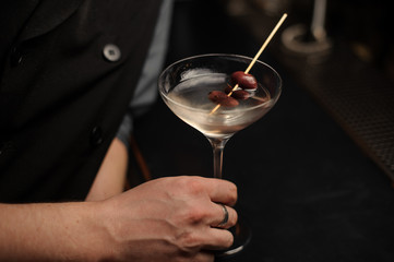 Close shot of alcohol cocktail with olives in bartender's hand