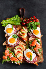 Appetizers table with healthy snacks. Brushetta or sandwich set on the board over black concrete background.