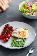 Blanched asparagus, fried egg, tomatoes and sald on the bowl. Breakfast concept