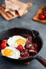 English breakfast of fried egg, tomatoes, bacon and toast on gray background
