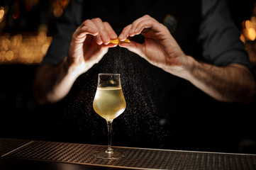 Bartedner holds lemon rind above alcohol cocktail
