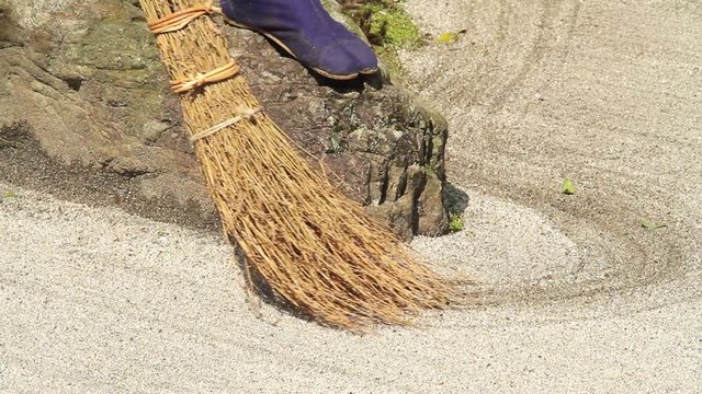 Groundsman standing on rock to sweep sand around rock at famous Meigetsu-in rock garden, Kita-Kamakura, Kanagawa, Japan