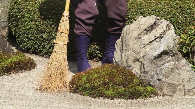 Medium close of legs of groundsman sweeping sand at famous Meigetsu-in rock garden