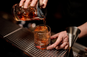 Bartender pouring alcohol cocktail using glass with strainer