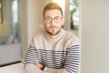 Young handsome man wearing glasses at home with serious expression on face. Simple and natural looking at the camera.