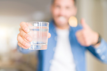 Young handsome man drinking a glass of water at home happy with big smile doing ok sign, thumb up with fingers, excellent sign