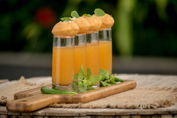 Pani Puri Shots : (a.k.a. golgappa shots or gol gappe shots) are a versatile snack invented in India made of stuffed pani puri (golgappa) placed on top of liquid-filled shot glasses. - obrazy, fototapety, plakaty