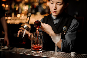 Bartender pouring alcohol cocktail with a jigger