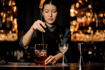 Female bartender stirring alcohol cocktail with bar spoon