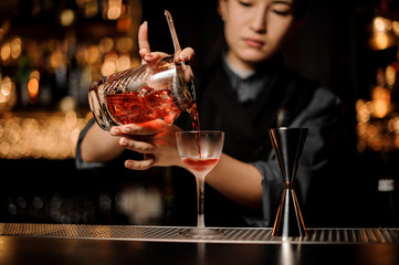 Bartender pours alcohol cocktail using the strainer