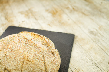 Close-up of a loaf of homemade bread with sesame seeds in selective focus on wooden table background