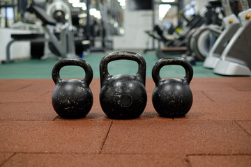 Naklejka na ściany i meble Тhree black iron kettlebells with markings 24 and 16 kg standing close to each other. Gym and fitness equipment. Workout tools