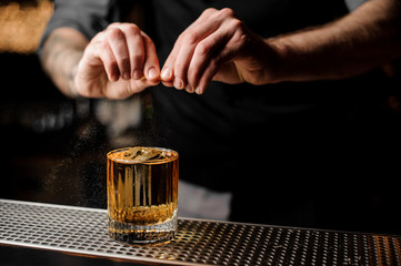 Bartender squeezes lemon rind in alcohol cocktail
