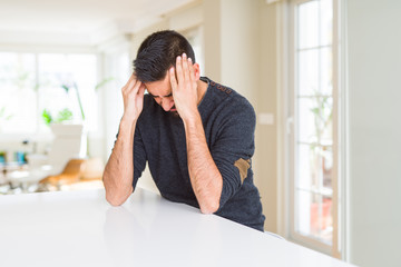 Handsome hispanic man wearing casual sweater at home suffering from headache desperate and stressed...