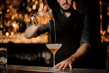 Male bartender makes alcohol cocktail using glass with strainer