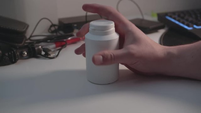 Quickly take two pills out of a unlabeled plastic bottle on cluttered desk.