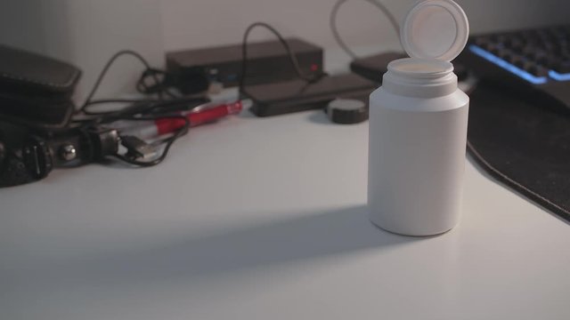 Quickly take a handfull of pills out of a unlabeled plastic bottle on cluttered desk.