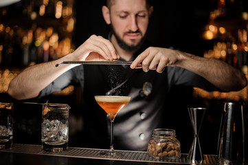 Bartender with beard pouring alcohol cocktail using grater