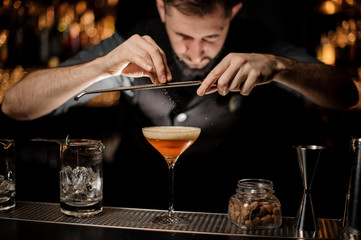 Bartender with beard pours an alcohol cocktail using grater
