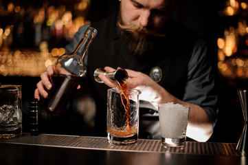 Male bartender pouring an alcohol cocktail with jigger