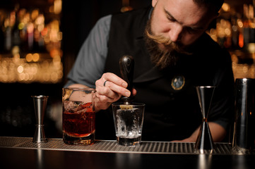 Male bartender adds ice in glass with ice picker