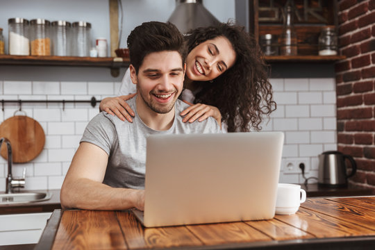 Picture of young couple looking at laptop on table while having breakfast in kitchen at home