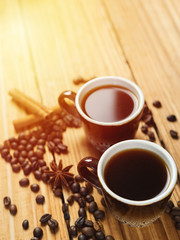 Two small cups of freshly brewed espresso on a wooden background with scattered coffee beans