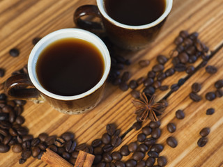 Two small cups of freshly brewed espresso on a wooden background with scattered coffee beans
