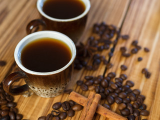 Two small cups of freshly brewed espresso on a wooden background with scattered coffee beans