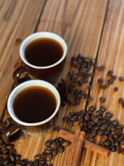 Two small cups of freshly brewed espresso on a wooden background with scattered coffee beans