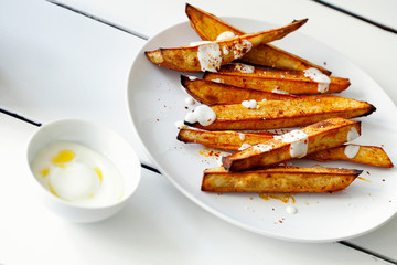 Homemade caramelized roasted sliced yams or sweet potato with Greek-style yogurt and crushed red-pepper flakes close-up on white wooden background.Healthy vegetable yummy side-dish
