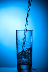 Pouring water into glass on blue background