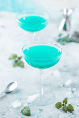 Colorful summer cocktail Blue Hawaii or iced blue lagoon alcohol drink with mint on light stone background