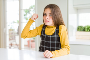 Young beautiful blonde kid girl wearing casual yellow sweater at home angry and mad raising fist frustrated and furious while shouting with anger. Rage and aggressive concept.