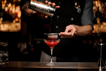Bartender using shaker and sieve to make cocktail