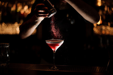 Male bartender sprinkles alcohol cocktail in a glass