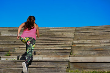 Mujer de espaldas corriendo en escaleras hacia fondo de cielo azul, copy-space