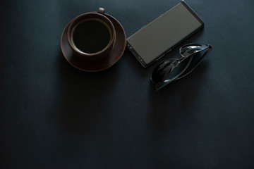 cup of coffee, sun glasses, smartphone on a black background