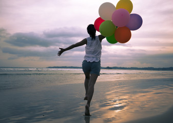 young asian woman running and jumping on seaside with colored balloons