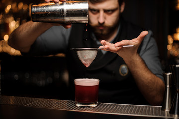 Bartender makes alcohol drink with a shaker and sieve