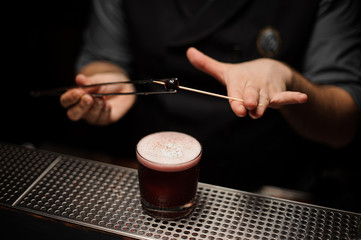 Fototapeta na wymiar Male bartender puts small cherry on toothpick with forceps
