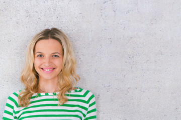 young, pretty blonde woman posing in front of a concrete wall and wearing green, white striped sweaters