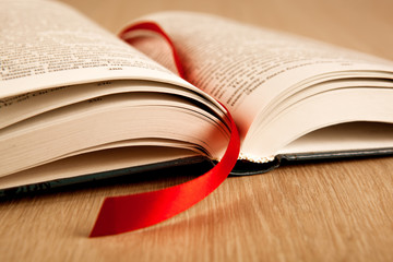 new open book on a wooden table with a red ribbon bookmark
