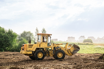 Obraz premium large yellow wheel loader aligns a piece of land for a new building