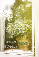 inscription Hello Summer on the background of a bouquet with daisies in a basket on rustic window