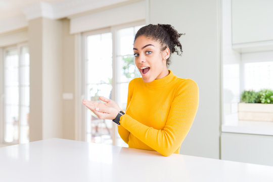 Beautiful african american woman with afro hair wearing a casual yellow sweater pointing aside with hands open palms showing copy space, presenting advertisement smiling excited happy
