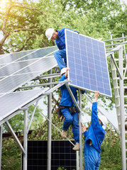 Installing of stand-alone solar photo voltaic panel system. Workers in hard-hats and blue overall...