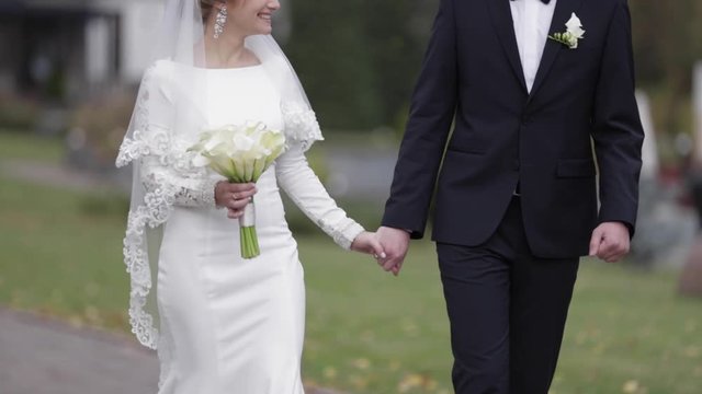 Happy newlyweds walking in the park. Elegant bride and handome groom outside