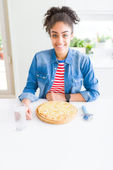 Young african american woman eating homemade cheese pizza with a happy face standing and smiling with a confident smile showing teeth